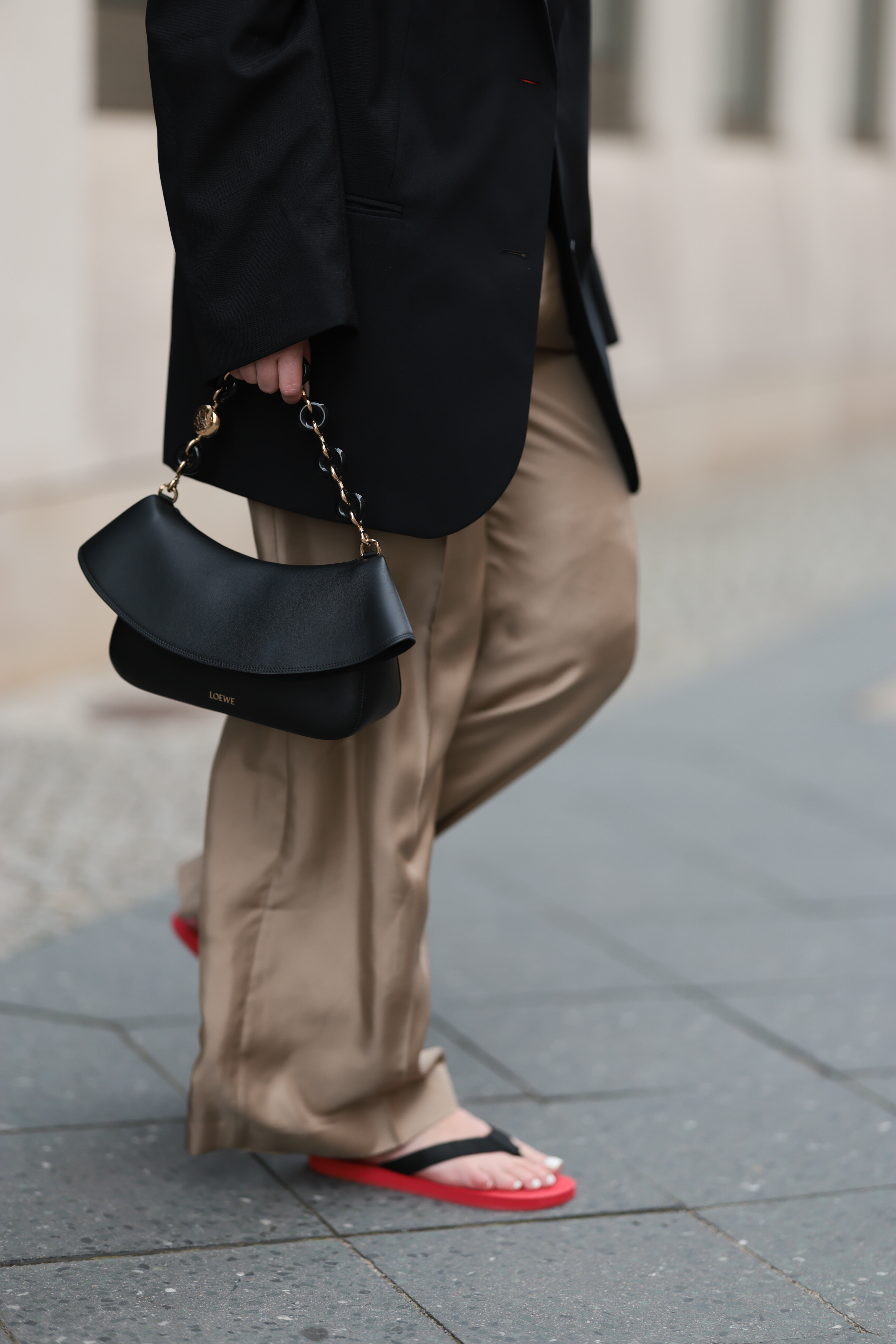 a woman wearing silk pants with the row flip flops and a chain handle bag