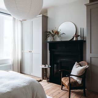 Light grey painted bedroom, built in wardrobes, black fireplace, armchair, double bed