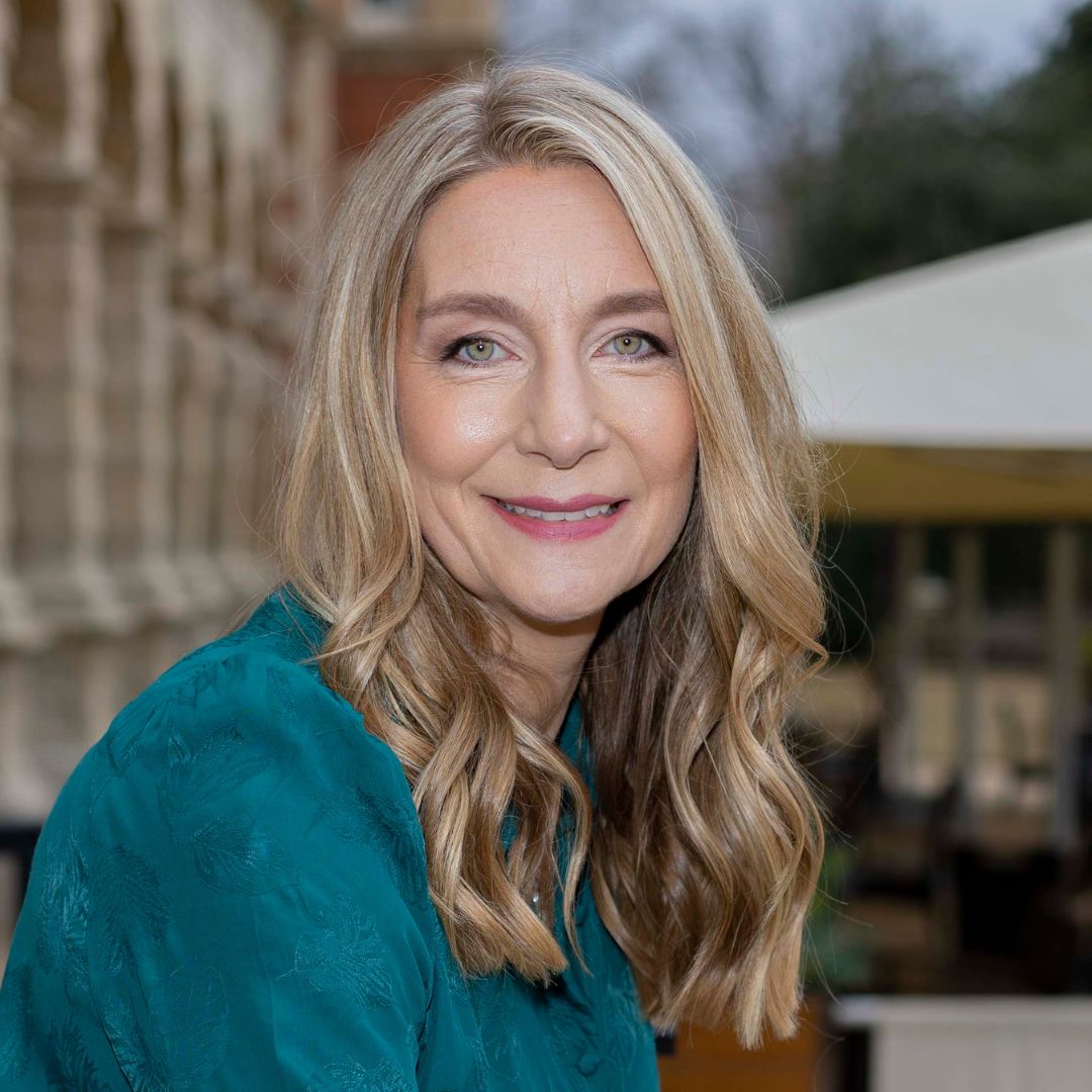 A blonde haired lady wearing a teal dress smiles at the camera