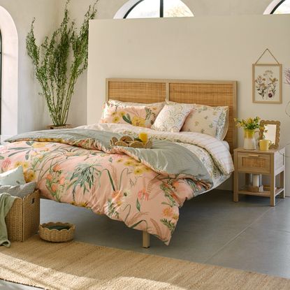 A bedroom with floral sheets on the bed and scalloped wicker accessories placed around the room