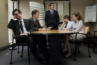 the dundermiflin employees sit around a table in a conference room in The Office