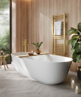 bathroom with wooden slatted effect walls, large white freestanding bath and large green plant to side of shot