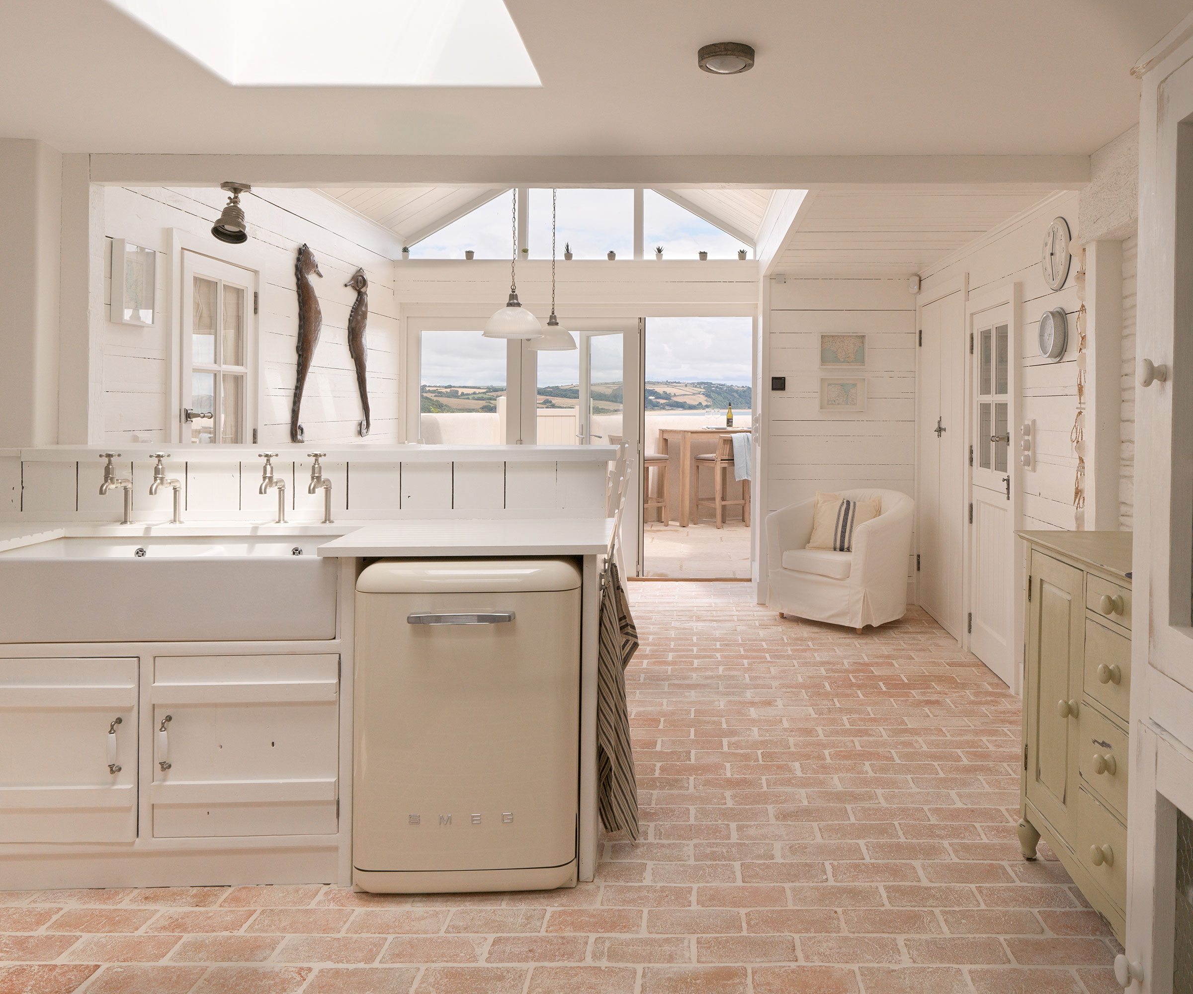 open plan white coastal kitchen with brick flooring and roof lantern