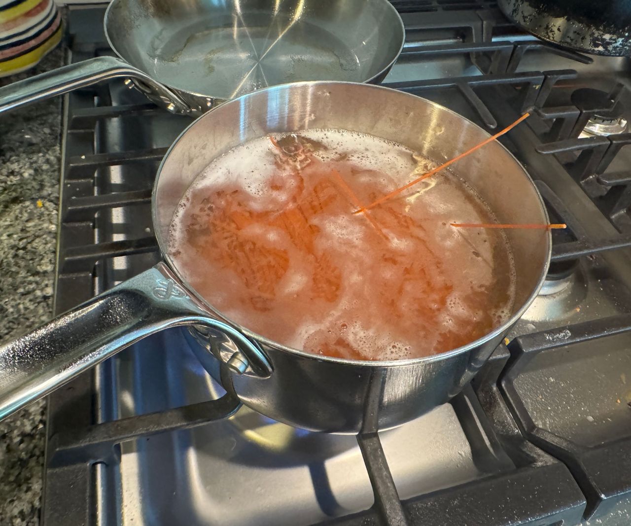 A stainless steel saucepan boiling pasta on a gas stove