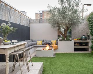 How to plan an outdoor kitchen shown in a town garden with built-in L-shaped seating, an olive tree and bar stools.