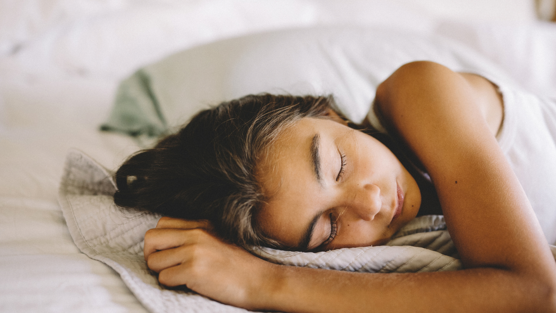 A teenager lies asleep on her side in bed in the morning.