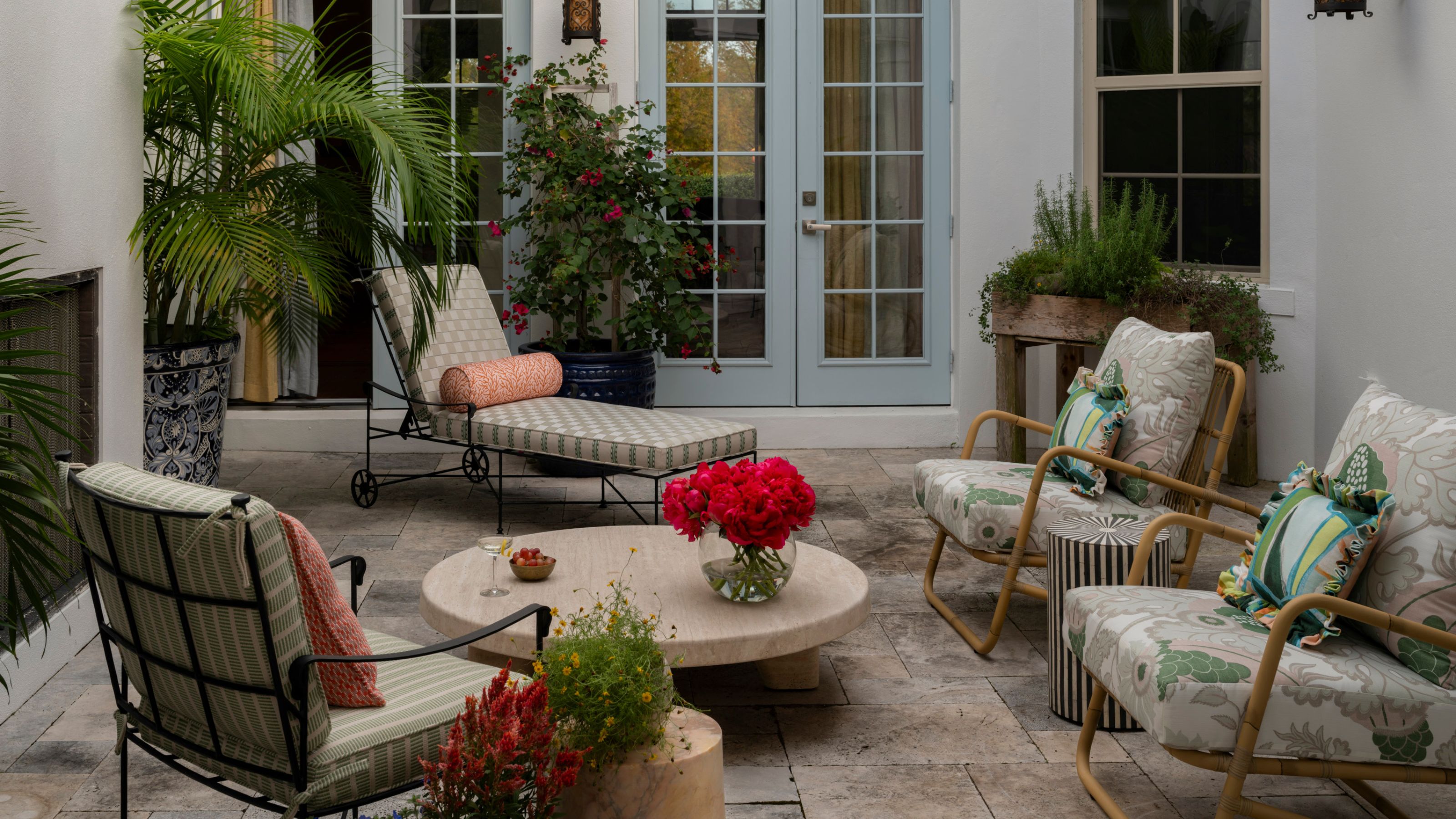 a large courtyard patio area with blue painted french doors and floral and stripe vintage style patio furniture