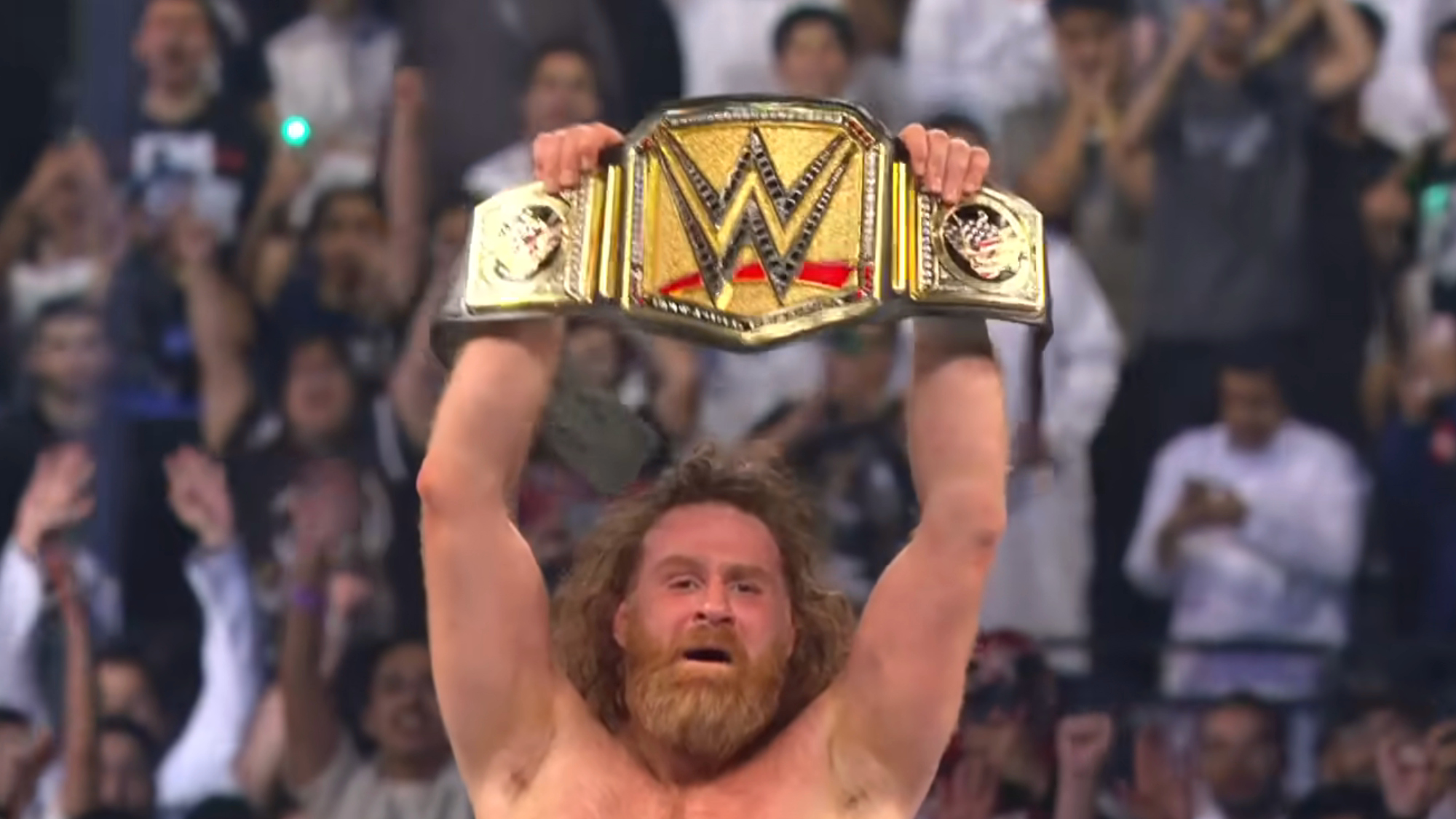 Sami Zayn celebrates after winning the WWE Championship by raising the belt in the air.