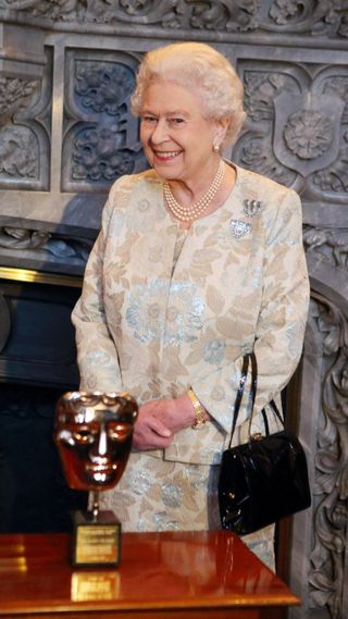 Queen Elizabeth posing behind a BAFTA award