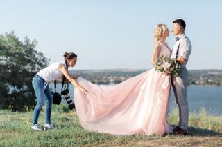 Photographer holding bride's train while bride embraces groom