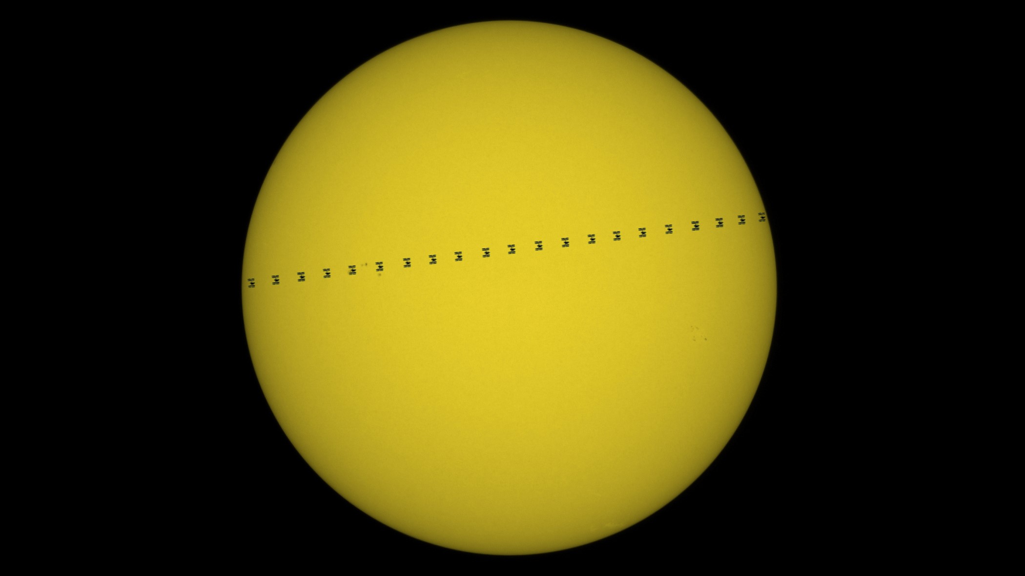 The International Space Station transiting the sun. Multiple images of the ISS spread across the solar surface like a line of ants crossing the screen.