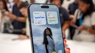 Apple iPhone 16 Pro smartphone held in hand showing screen with people in background