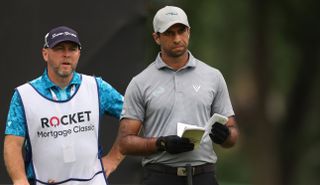 Aaron Rai looks at his yardage book whilst speaking to his caddie
