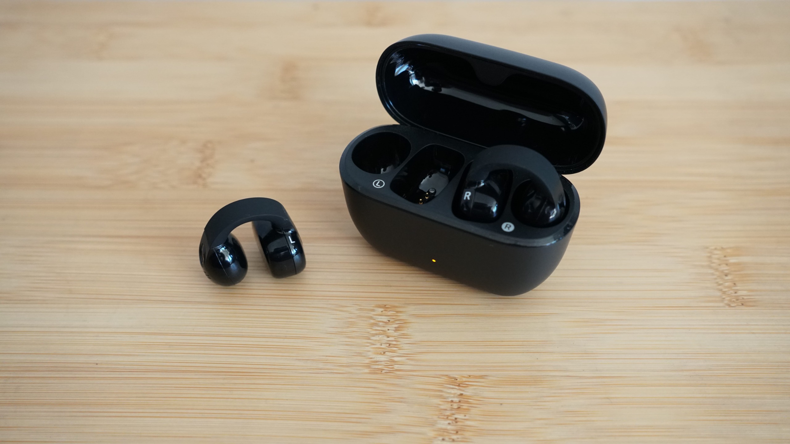 Sennheiser's Accentum Clip held in a hand, over a wooden table, with the case visible