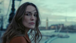 kiera knightley as helen turning over her shoulder and standing by the river in london in black doves