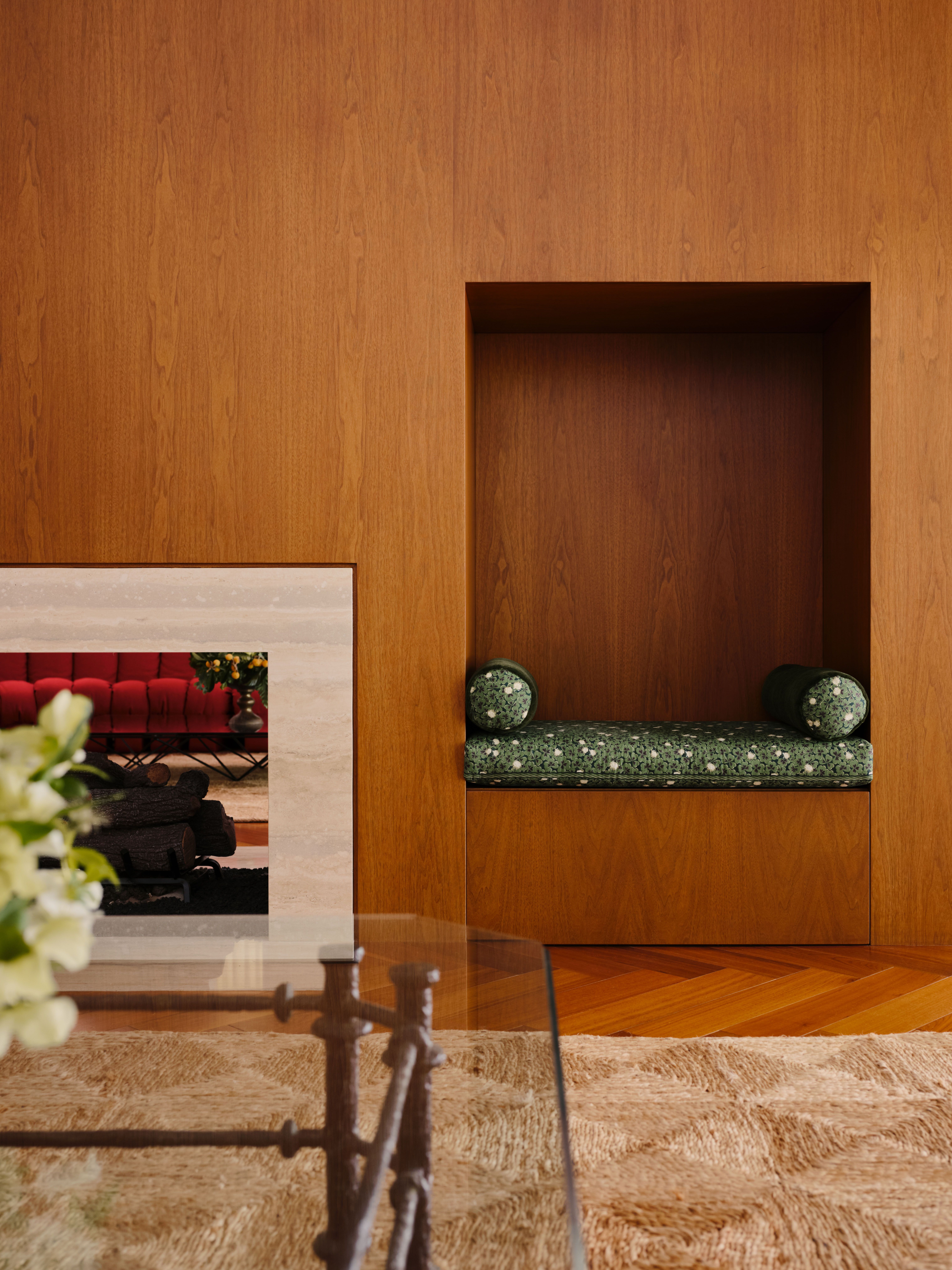 Wood-clad living room wall with a built-in seat with cylindrical cushions and mat and a see-through fire place framed by marble