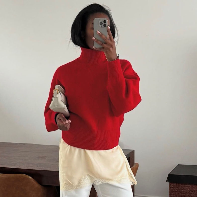 A woman wearing a red sweater, white pants, and red sandals