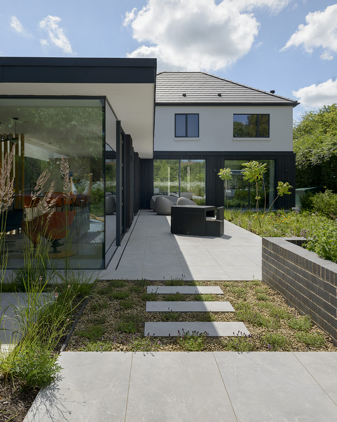 Neatly landscaped rear garden of a 1930s home renovation and extension. There is porcelain paving and some gravel garden patches