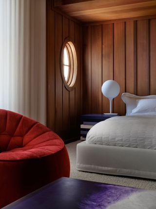 a bedroom with a red chair, wood walls and a wood ceiling