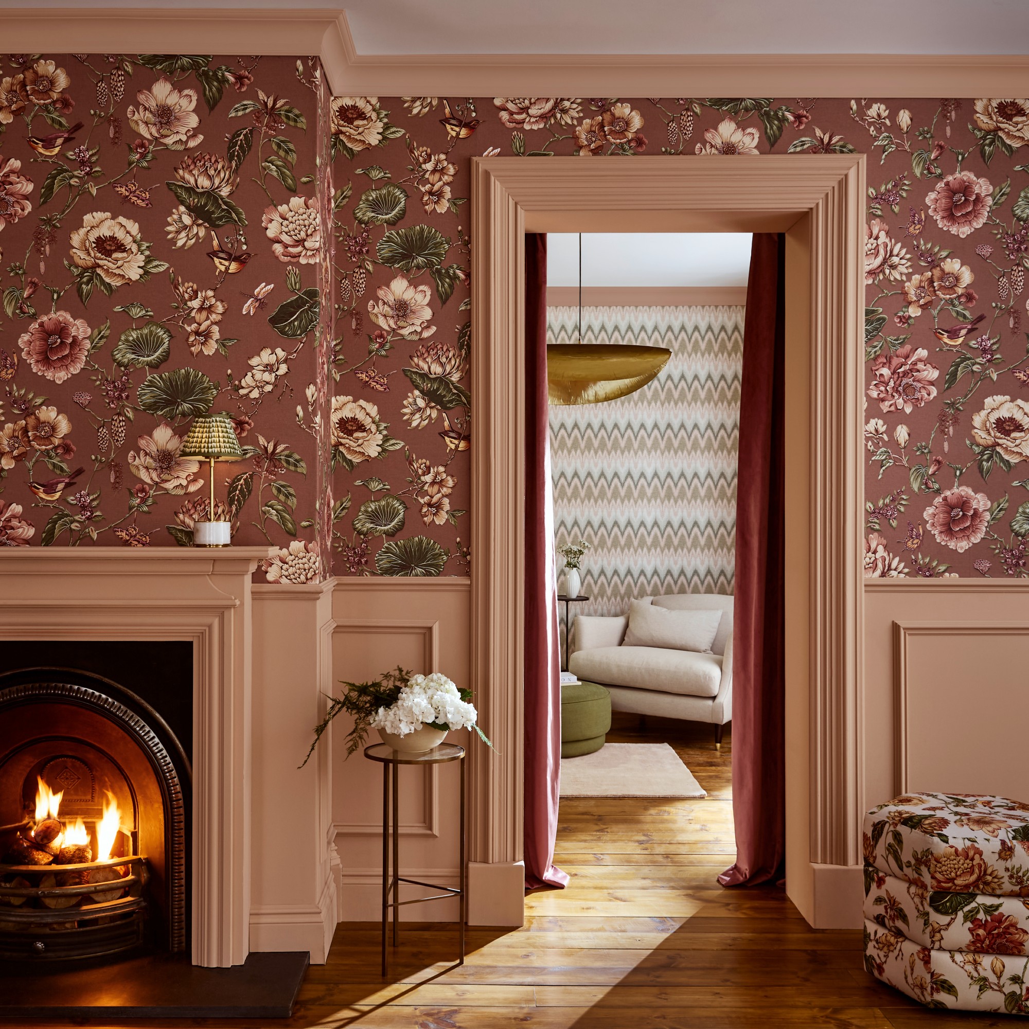 A pink bedroom with dado rail wall panelling and fireplace painted in Graham &amp;amp; Brown's Rose Earth pink shade and the upper wall covered in the Roselle Grove wallpaper