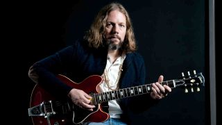 Ric h Robinson of the Black Crowes seated and holding a guitar