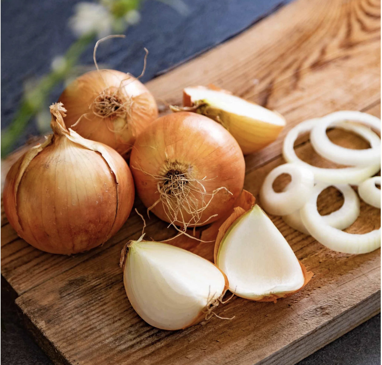 Three whole onions and several onion pieces on a wooden board