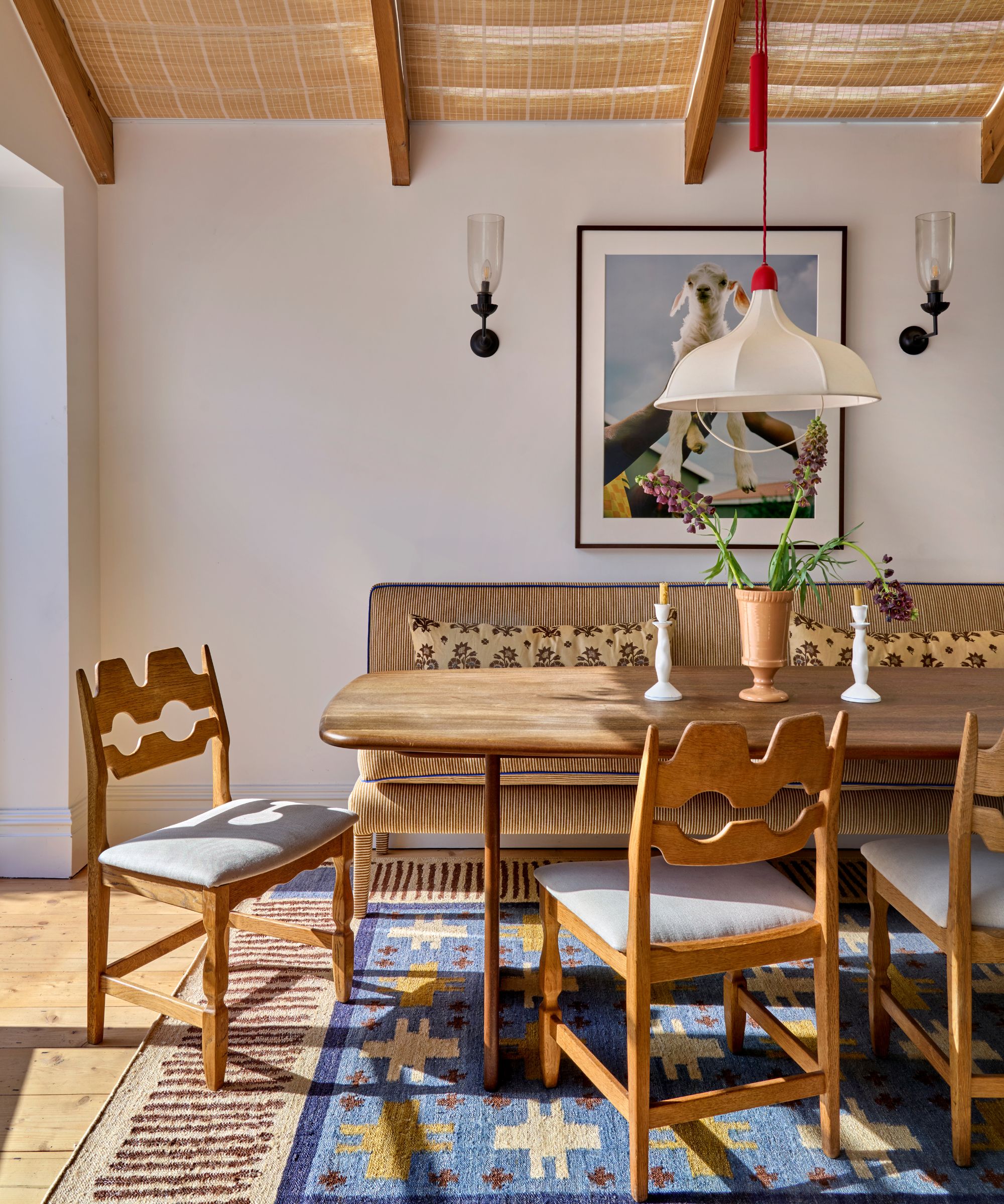breakfast nook banquette dining space in fashion influencer lucy williams' home with a striped ochre upholstered banquette, pine table, vintage razor pine chairs, and a blue and striped rug