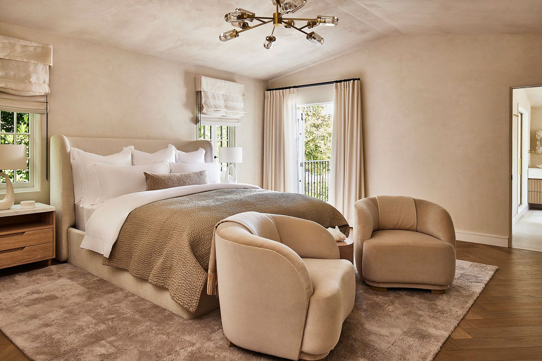 Beige bedroom with oatmeal tones in drapes, throws, and slouchy armchairs at the foot of the bed