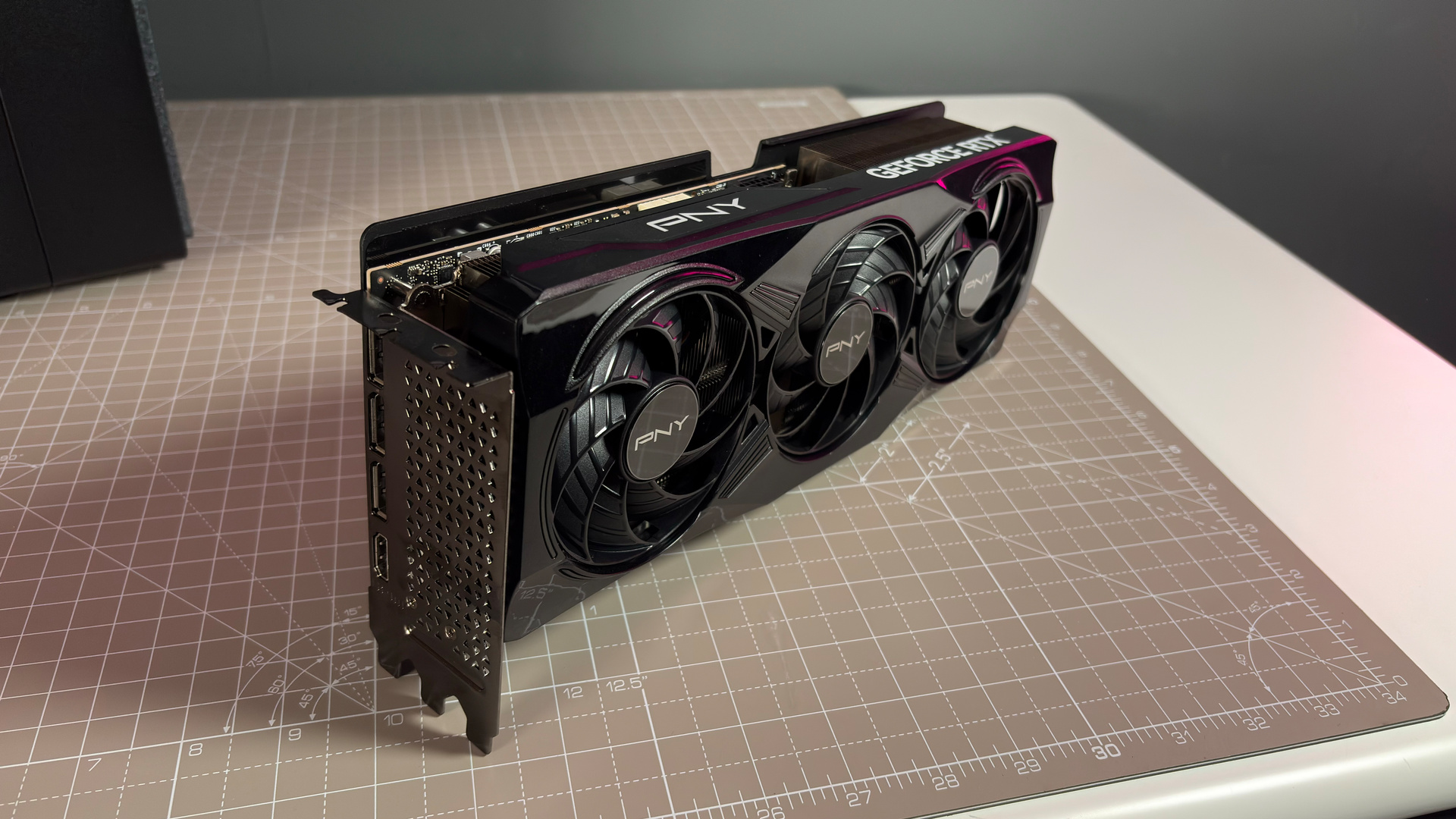 A PNY RTX 5070 Ti OC graphics card on a desk with a desk mat and pink light.