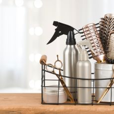 Side view of a basket of hair products and styling tools sat on a wooden surface 