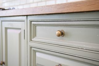 A mint green kitchen cabinet with brass handles