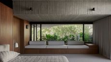 brutalist style bedroom with timber wall, concrete ceiling, bed, window seat, and planter box outside the window filled with verdant foliage