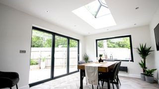 Extension with table and chairs on a wooden floor and Korniche roof lantern and bifold doors