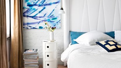 White bedroom with blue artwork and exposed brick wall painted white