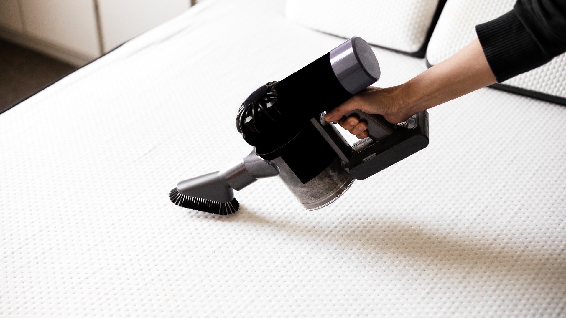 person hoovering their mattress with a handheld vacuum