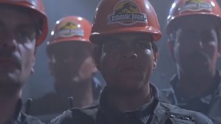 4 workers in orange hardhats with "Jurassic Park" on them looking nervous.