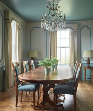 blue and cream dining room with wooden dining table and chairs, wooden herringbone flooring and chandelier