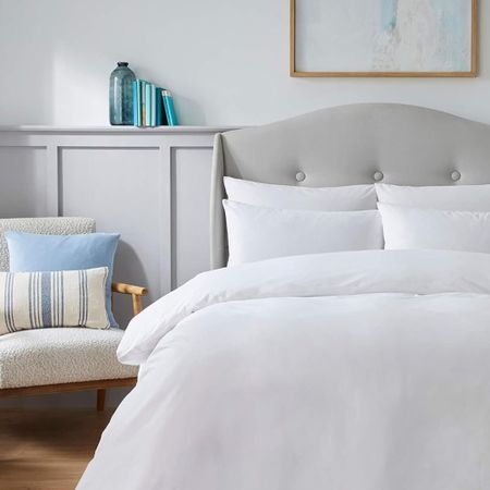 A bedroom with a bed covered in white bedlinen and a wooden armchair to one side