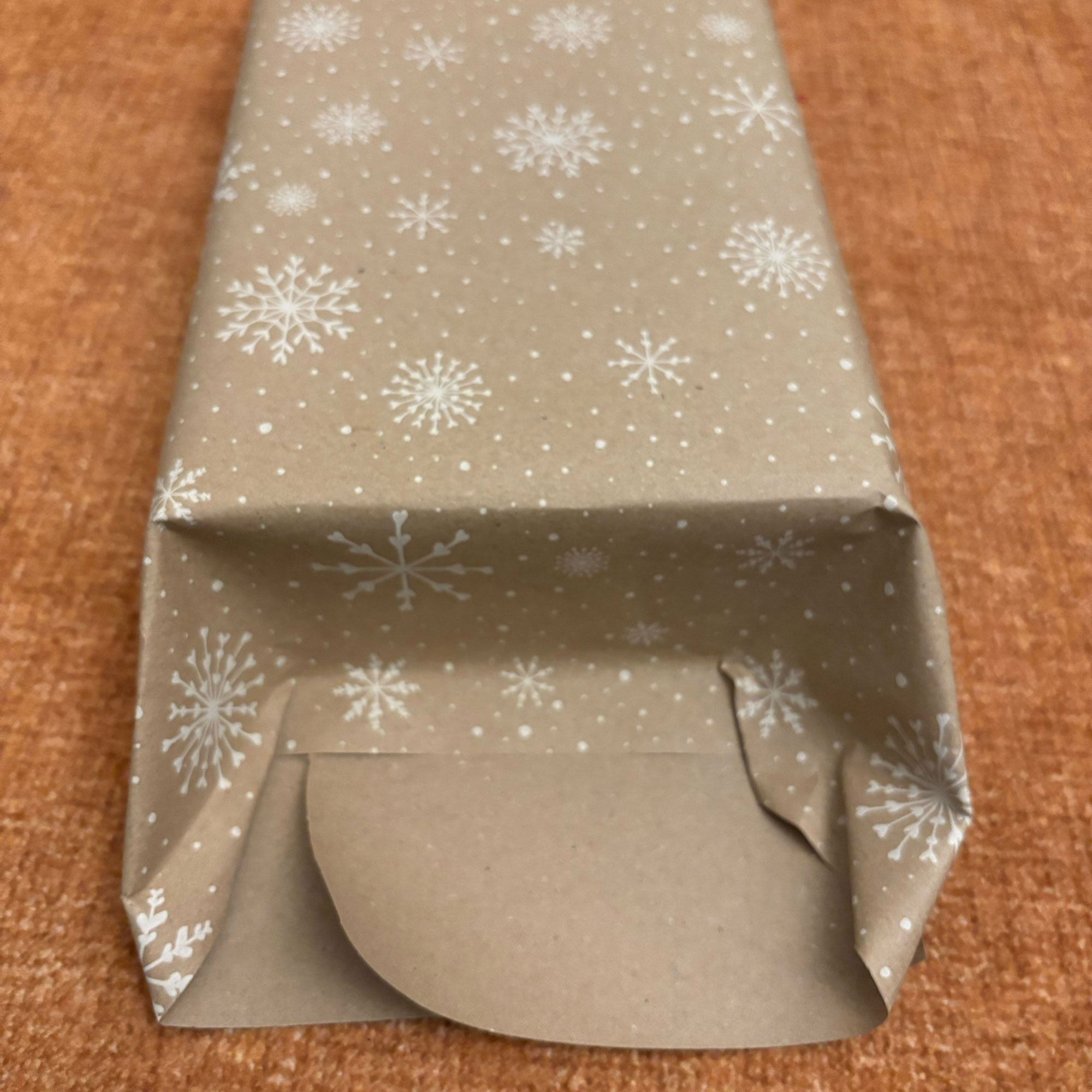 A rectangular box wrapped in brown paper with a white snowflake print on it