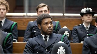 John Boyega as Leroy Logan wearing a police uniform sitting on jury duty with other officers.