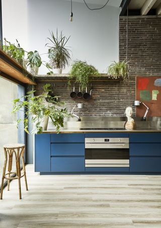 Blue kitchen ideas featuring mid blue painted base cabinets with chrome backsplash and fittings, in a large warehouse-style rom with exposed brick walls.