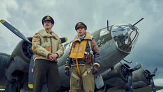Two pilots stand in front of a World War 2 era plane