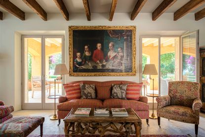 living room with russet colored sofa with two doorways behind and ceiling beams with large painting behind sofa 