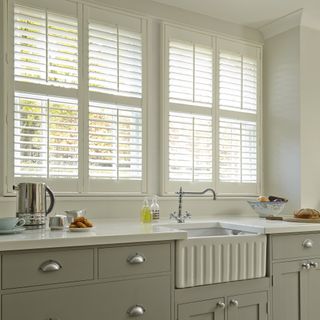 Grey shaker kitchen with white belfast sink and window with white shutters.