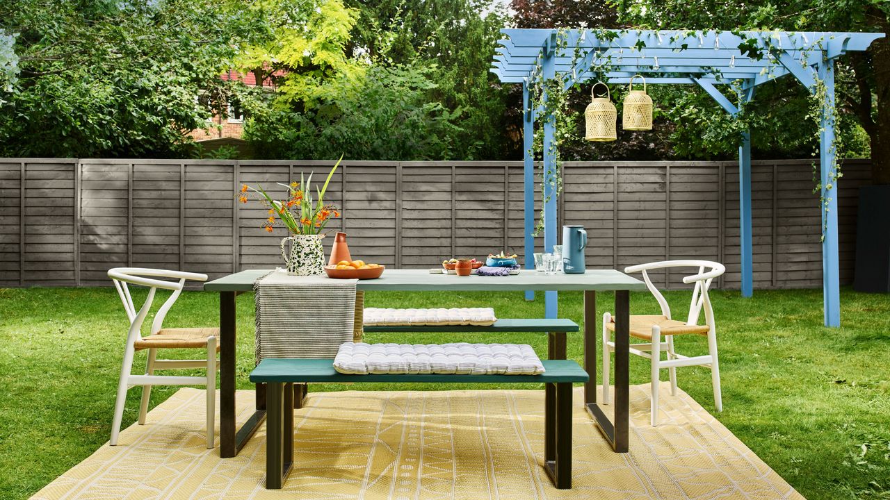 Grey painted garden fence with garden bench and table seating and blue pergola