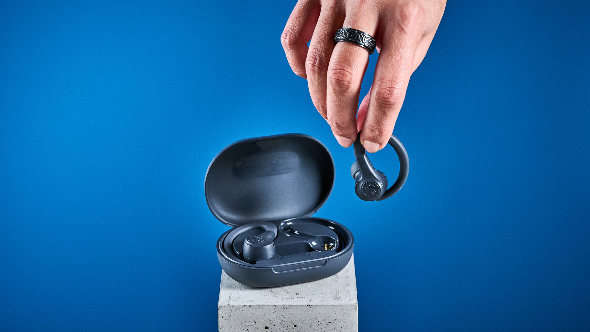 the jlab go sport+ earbuds photographed against the blue tom's guide background, showing charging case and wearing style