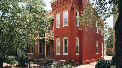 a large red brick Georgetown Victorian townhouse with large bay windows, heritage window and brick detailing and a front yard area