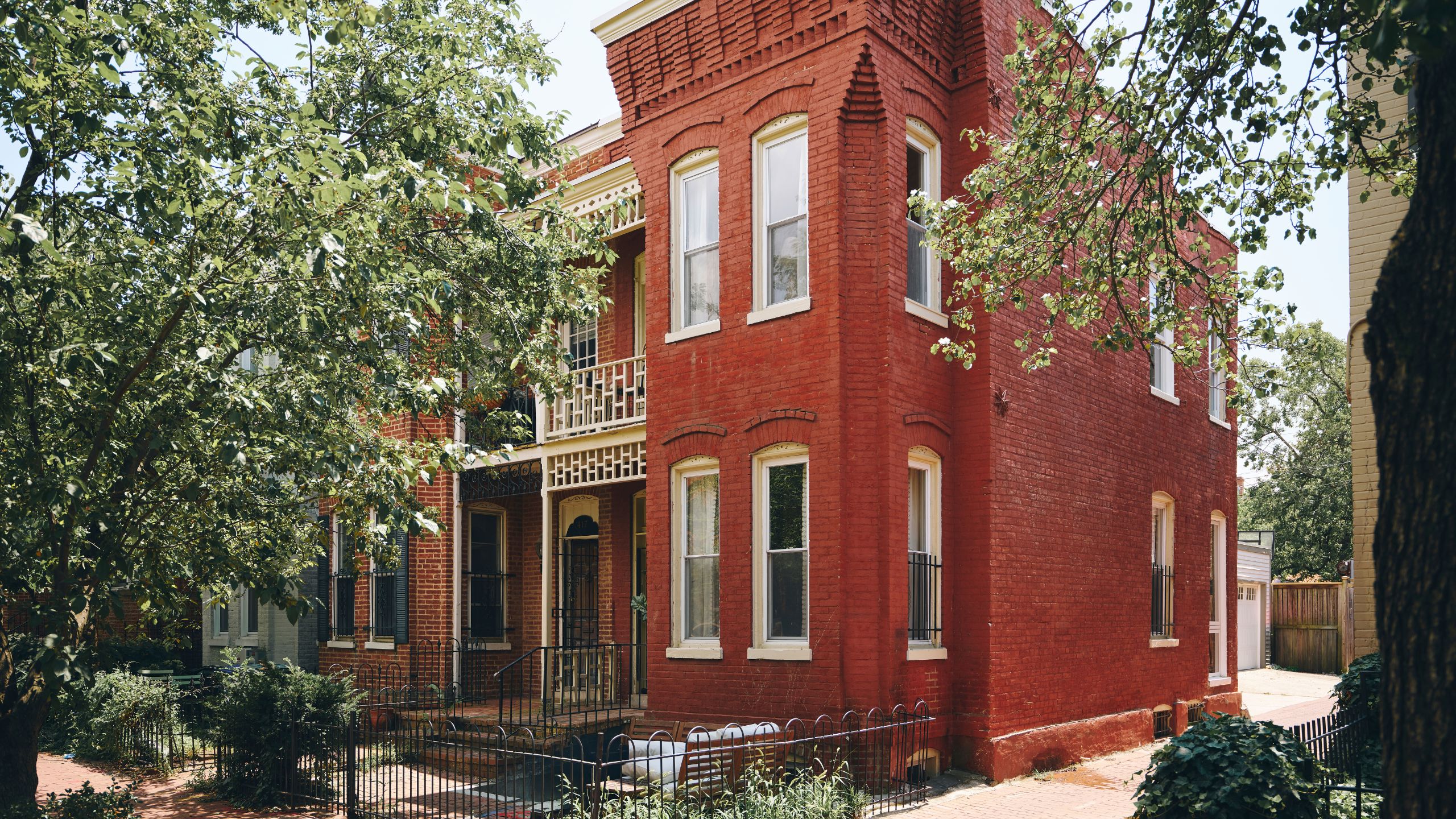 a large red brick Georgetown Victorian townhouse with large bay windows, heritage window and brick detailing and a front yard area