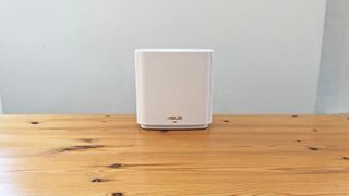 En vit Asus ZenWiFi AX (XT8) står placerad på ett träbord mot en vit bakgrund.