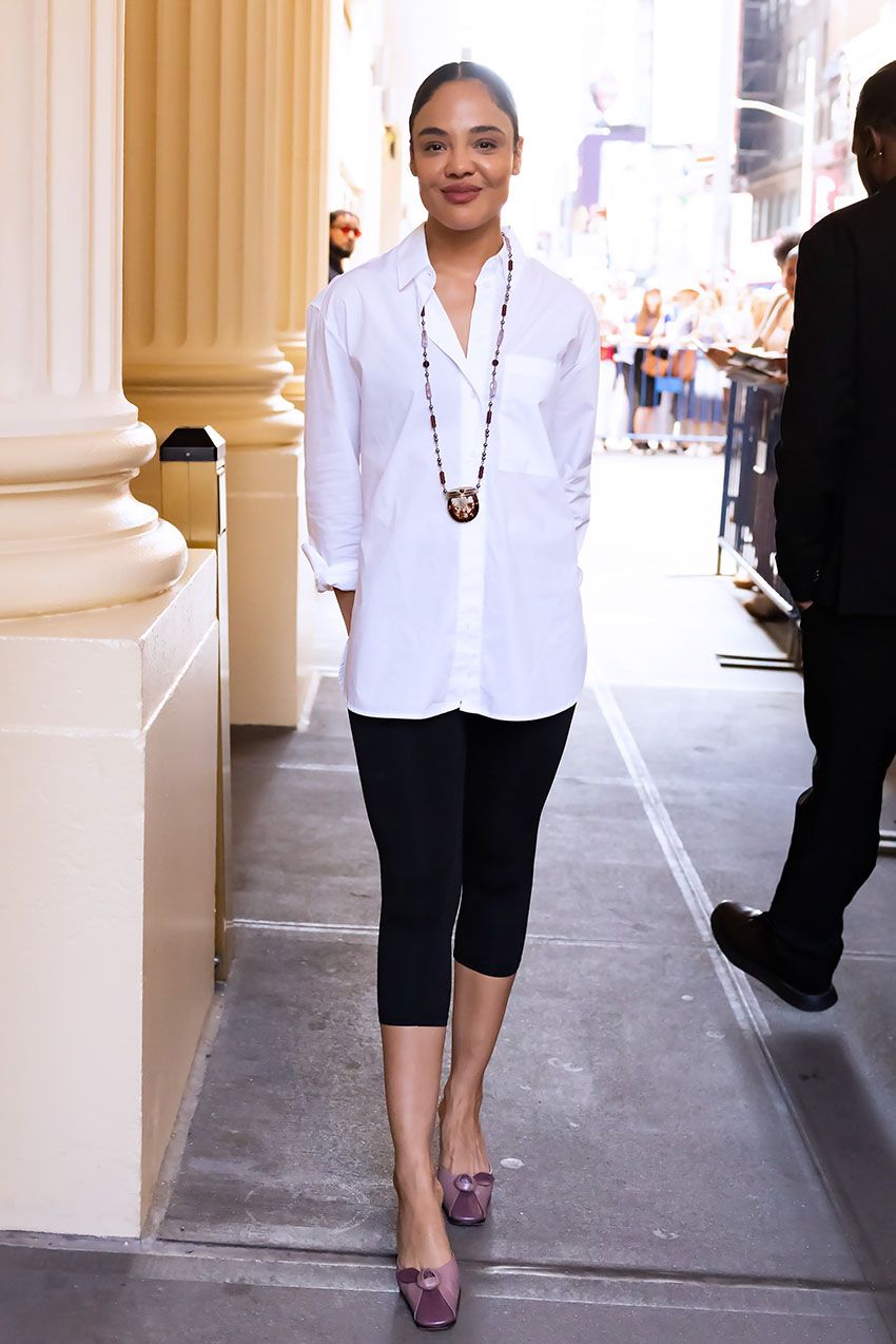 Tessa Thompson wearing a white button-dwon, black capri leggings, and purple mule heels